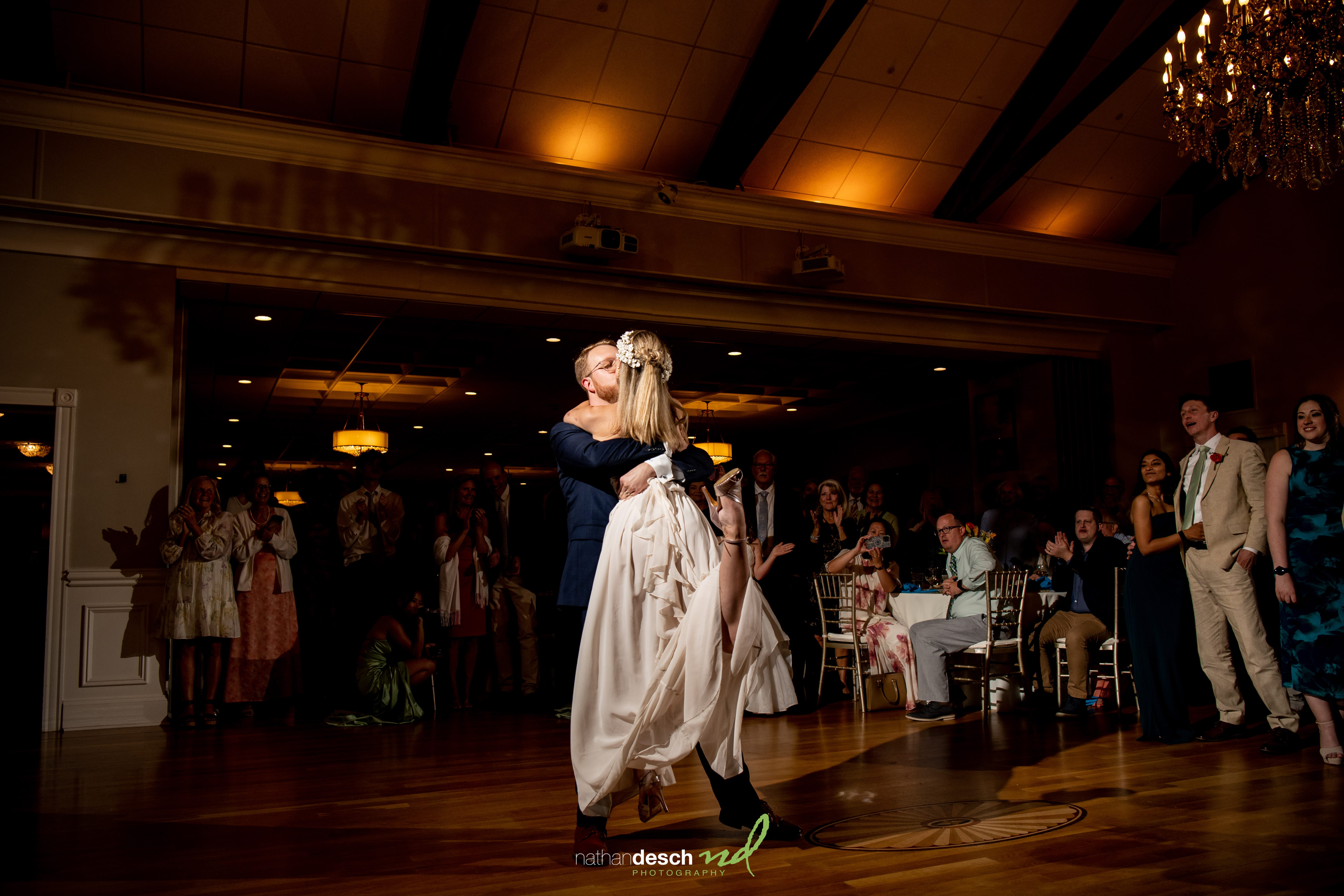 Bride and groom share their first dance at a warmly lit University and Whist Club wedding as guests watch and applaud.