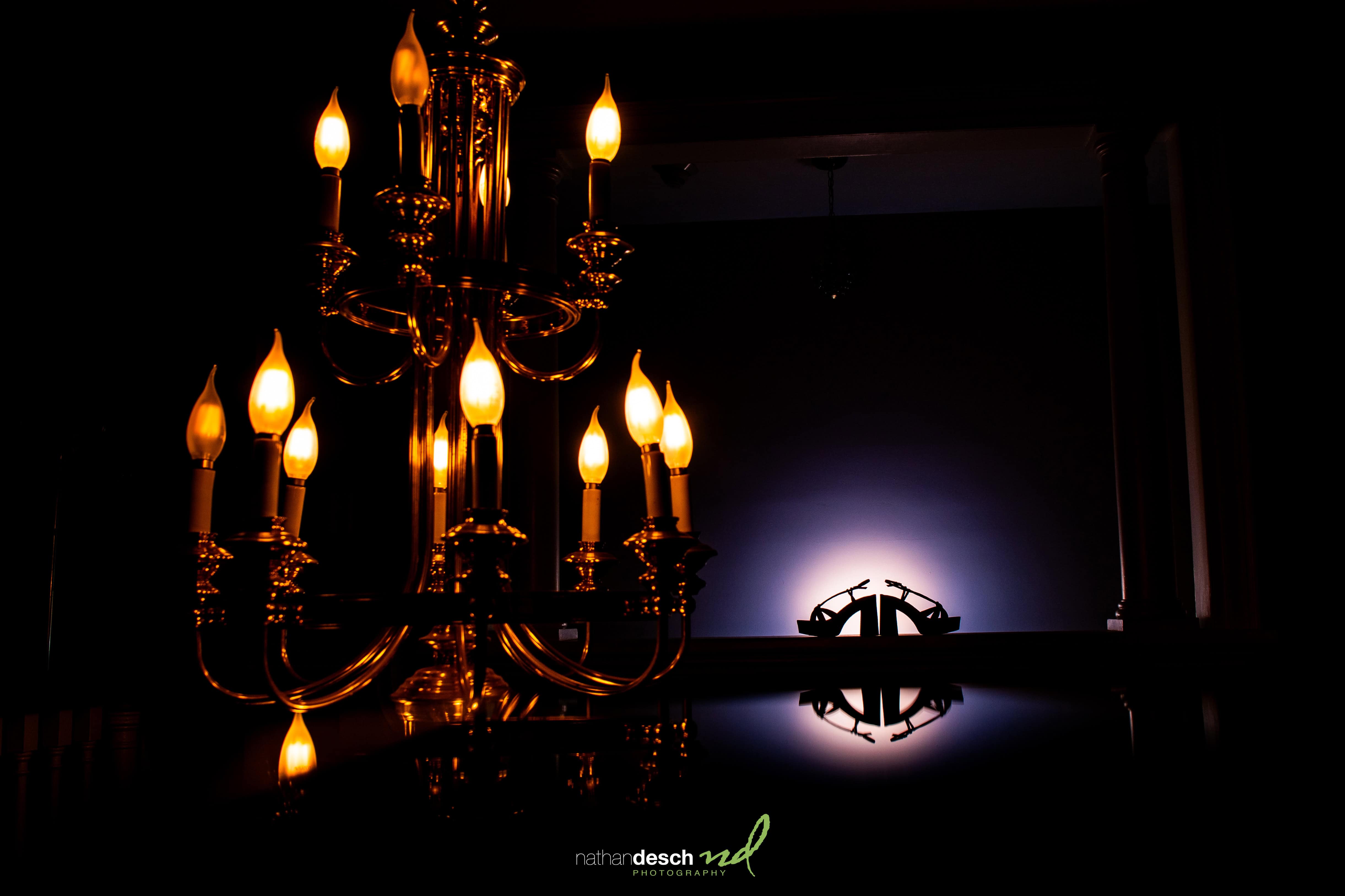 Elegant gold chandelier glows in a dark room with wedding rings illuminated on the wall at University and Whist Club wedding.