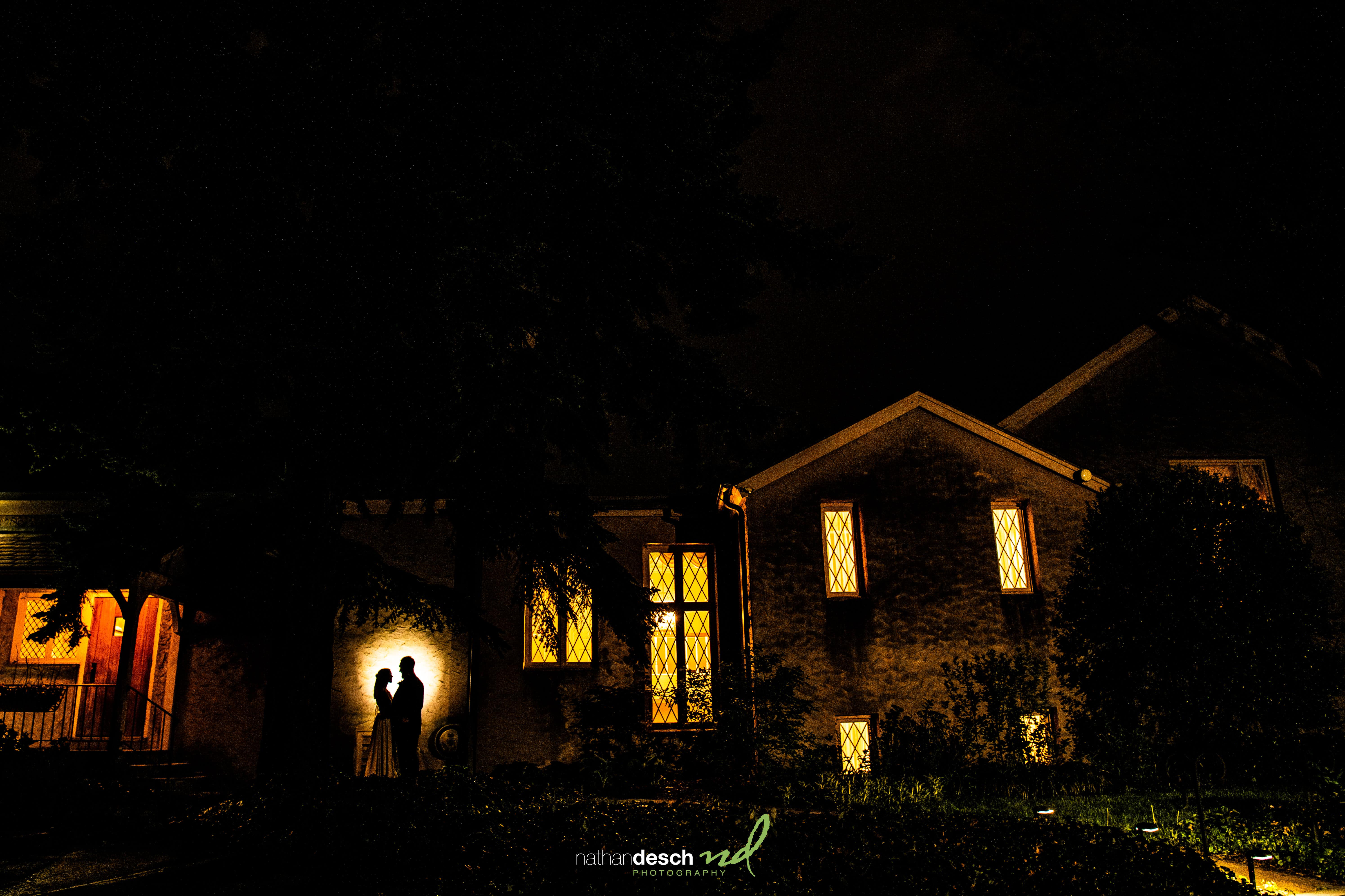 Silhouetted couple, Garrett and Ashley, embrace outside warmly lit house at night after their romantic University and Whist Club wedding.