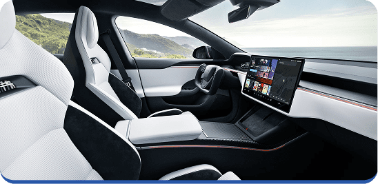 Interior view of a modern car featuring white leather seats, a minimalist dashboard, a unique rectangular steering wheel, and a large touchscreen display, with a scenic coastal landscape visible through the windows.