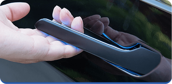 A close-up of a person’s hand reaching under a sleek, modern car door handle on a shiny black vehicle.