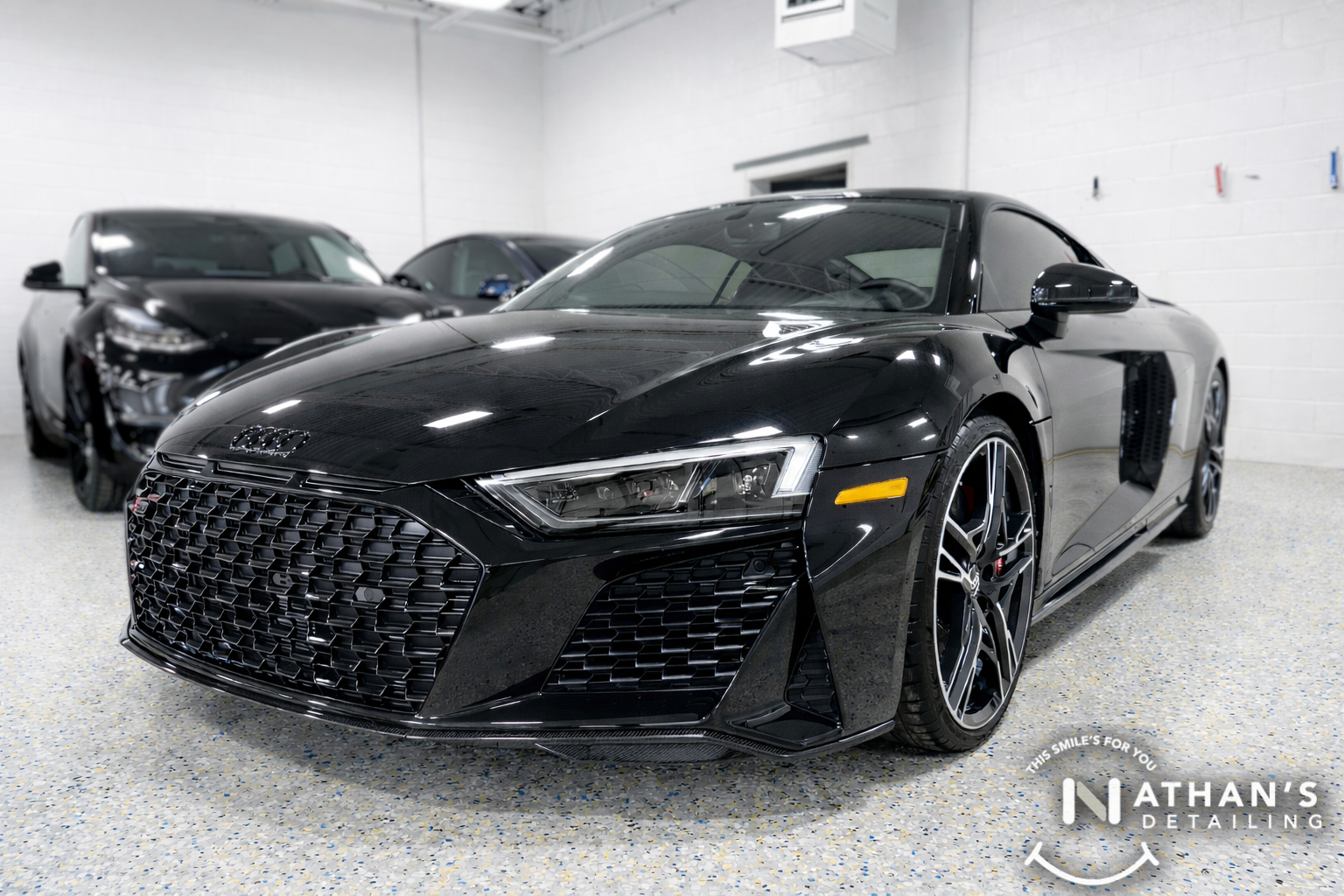 A sleek black Audi R8 in a clean detailing bay, showcasing the mirror-like reflections of a high-end ceramic coating.
