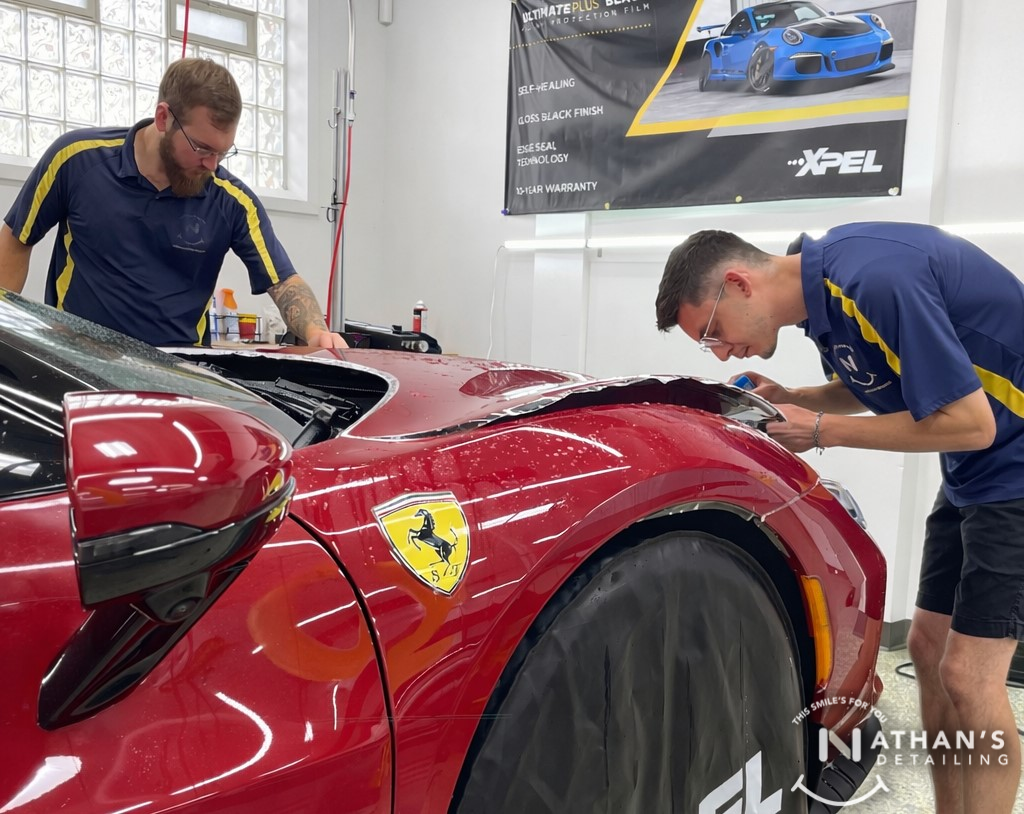 Technician applying paint protection film along the side of a Ferrari.