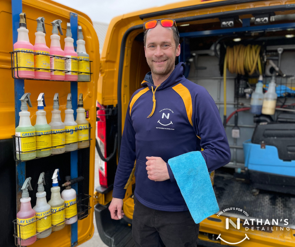 Mobile detailing technician standing beside an open van stocked with detailing products and microfiber towels.