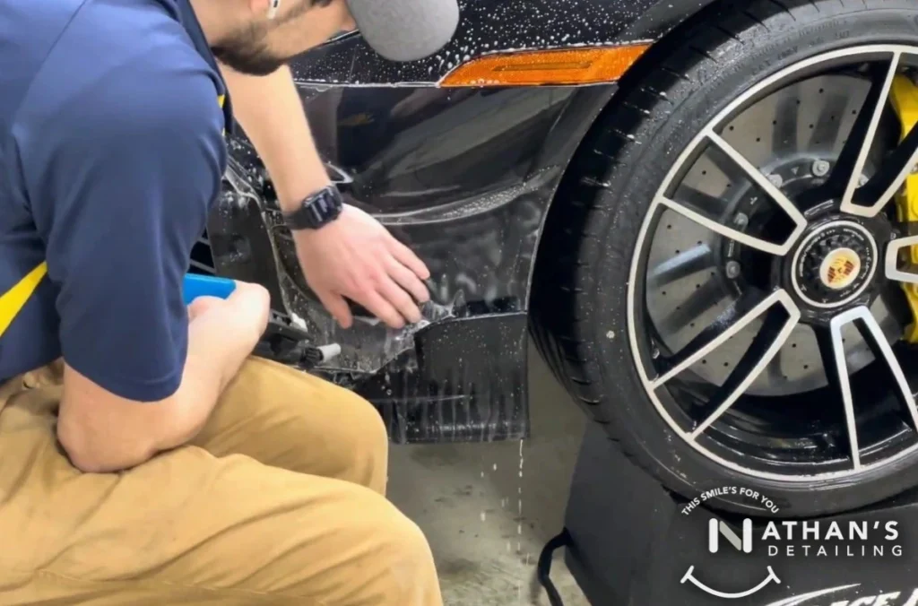 Technician applying paint protection film to the lower side panel of a porsche front bumper