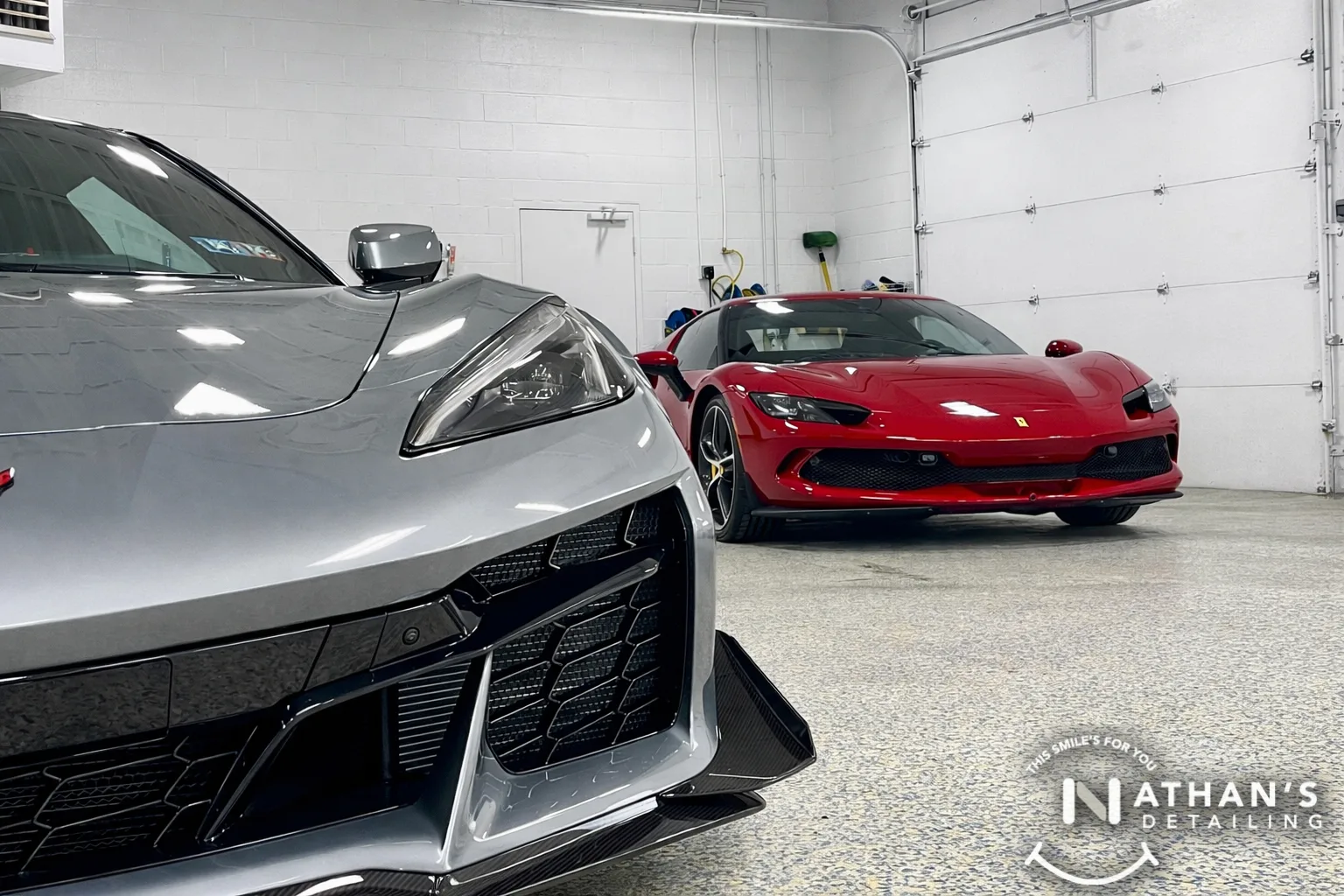 A silver sports car and a red Ferrari are parked inside a clean, well-lit detailing garage with white walls and a speckled floor. The Nathans Detailing logo is visible in the bottom right corner.