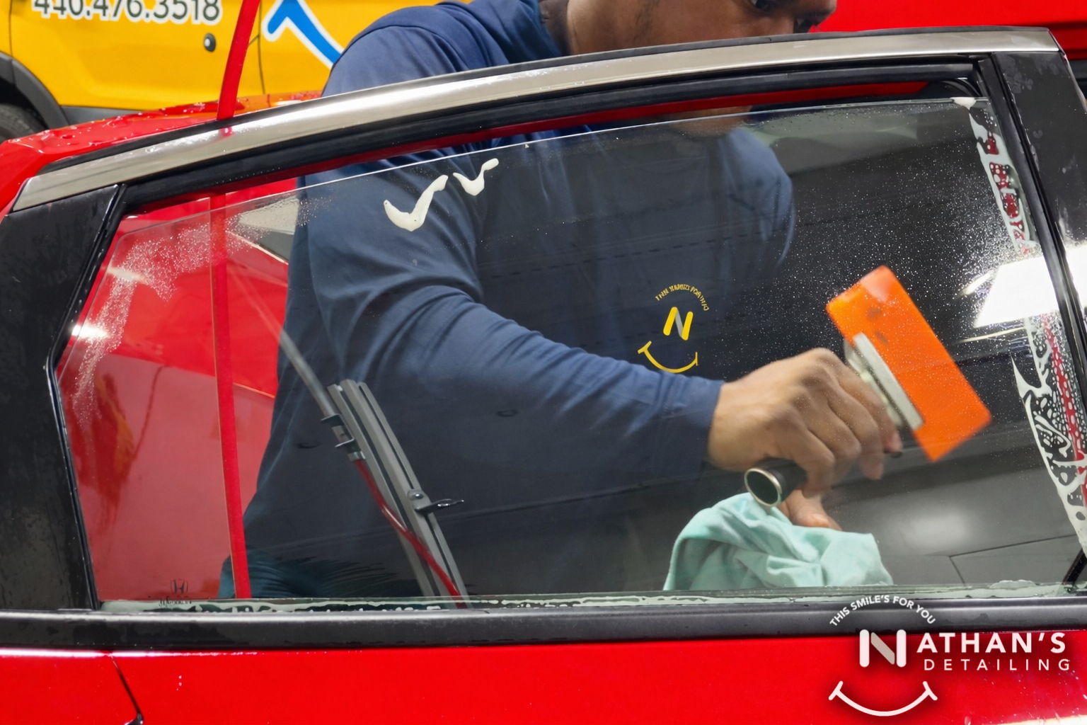 Preparing a car window for tint with a squeegee and microfiber towel on a red vehicle.