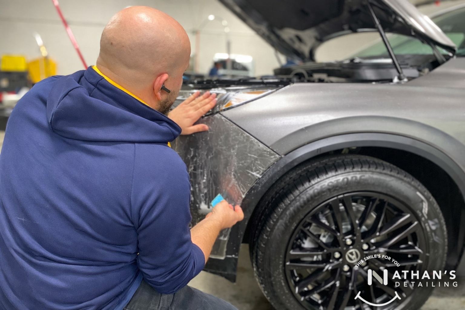 Technician applying paint protection film to a front fender using a squeegee.