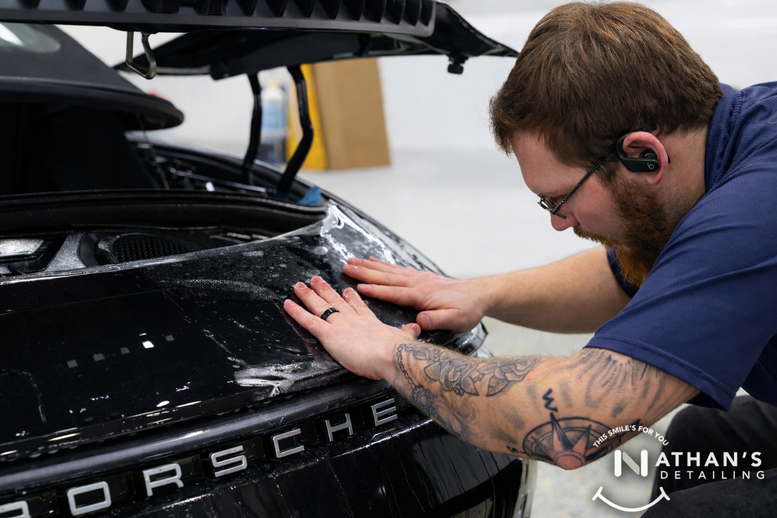 Technician smoothing paint protection film on the front panel of a Porsche.