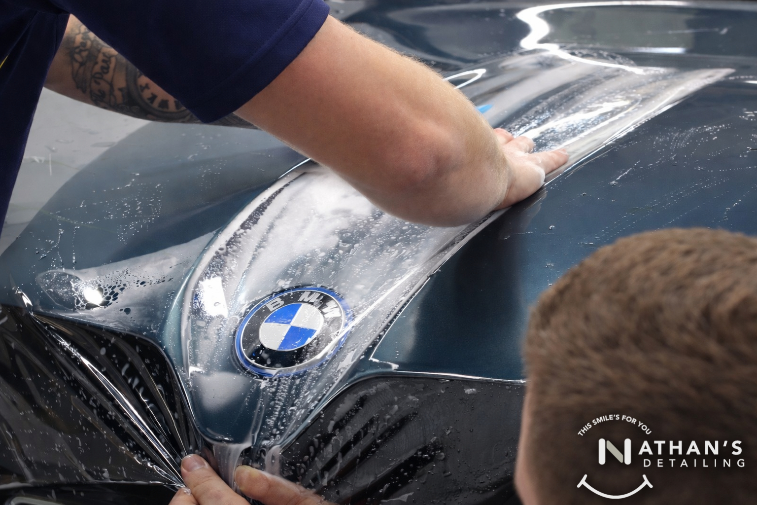 Installer smoothing paint protection film over the hood of a BMW.