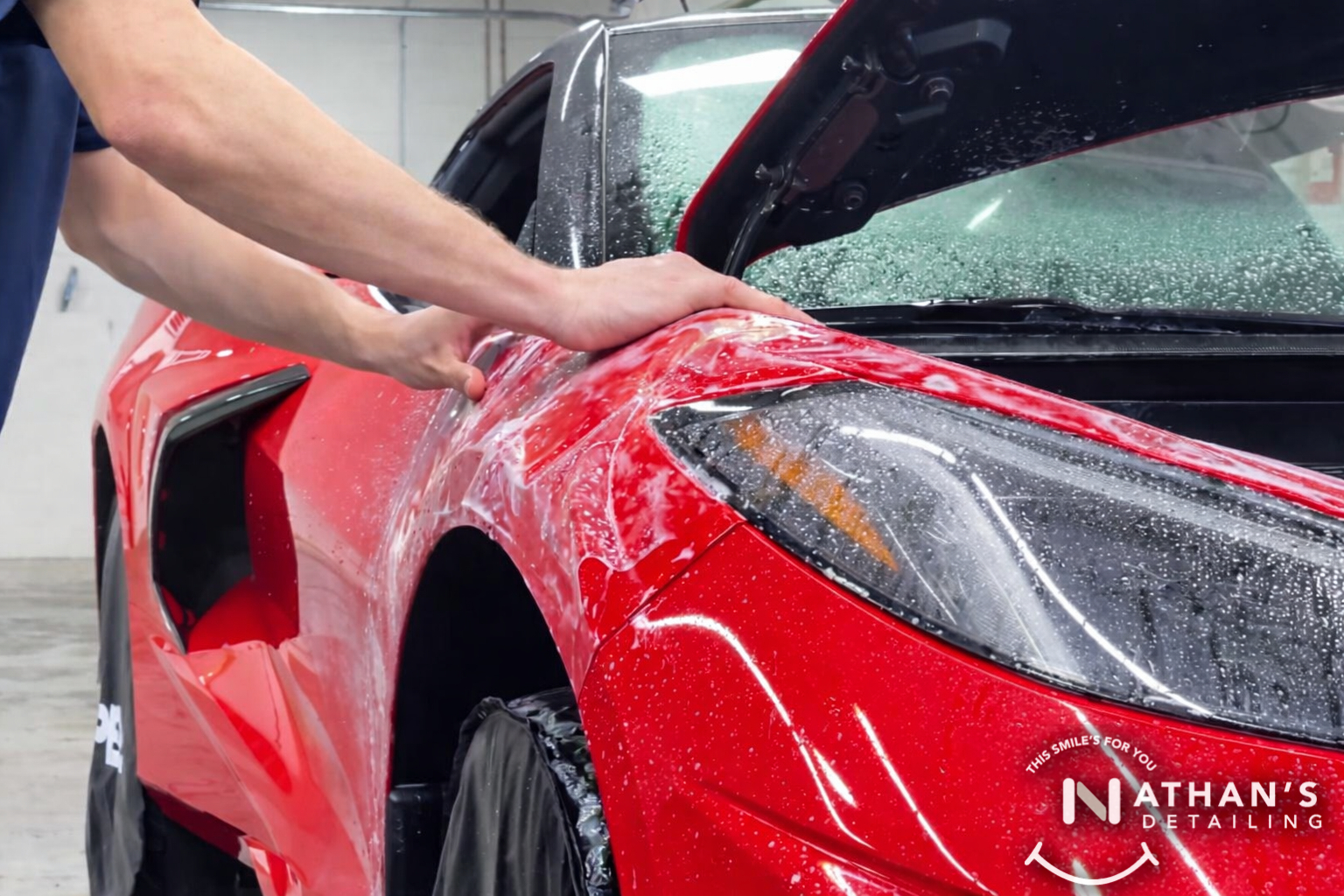 Hands smoothing paint protection film over a red fender during installation.