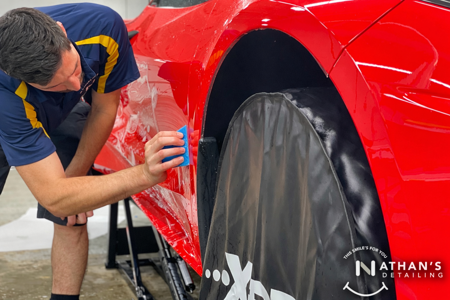 Installer squeegeeing paint protection film around a red wheel arch.