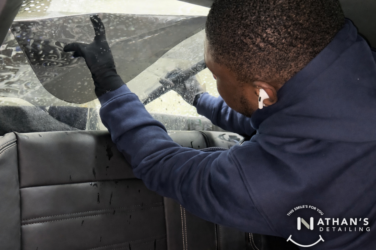 Installer placing window tint film on a rear window from inside the vehicle.