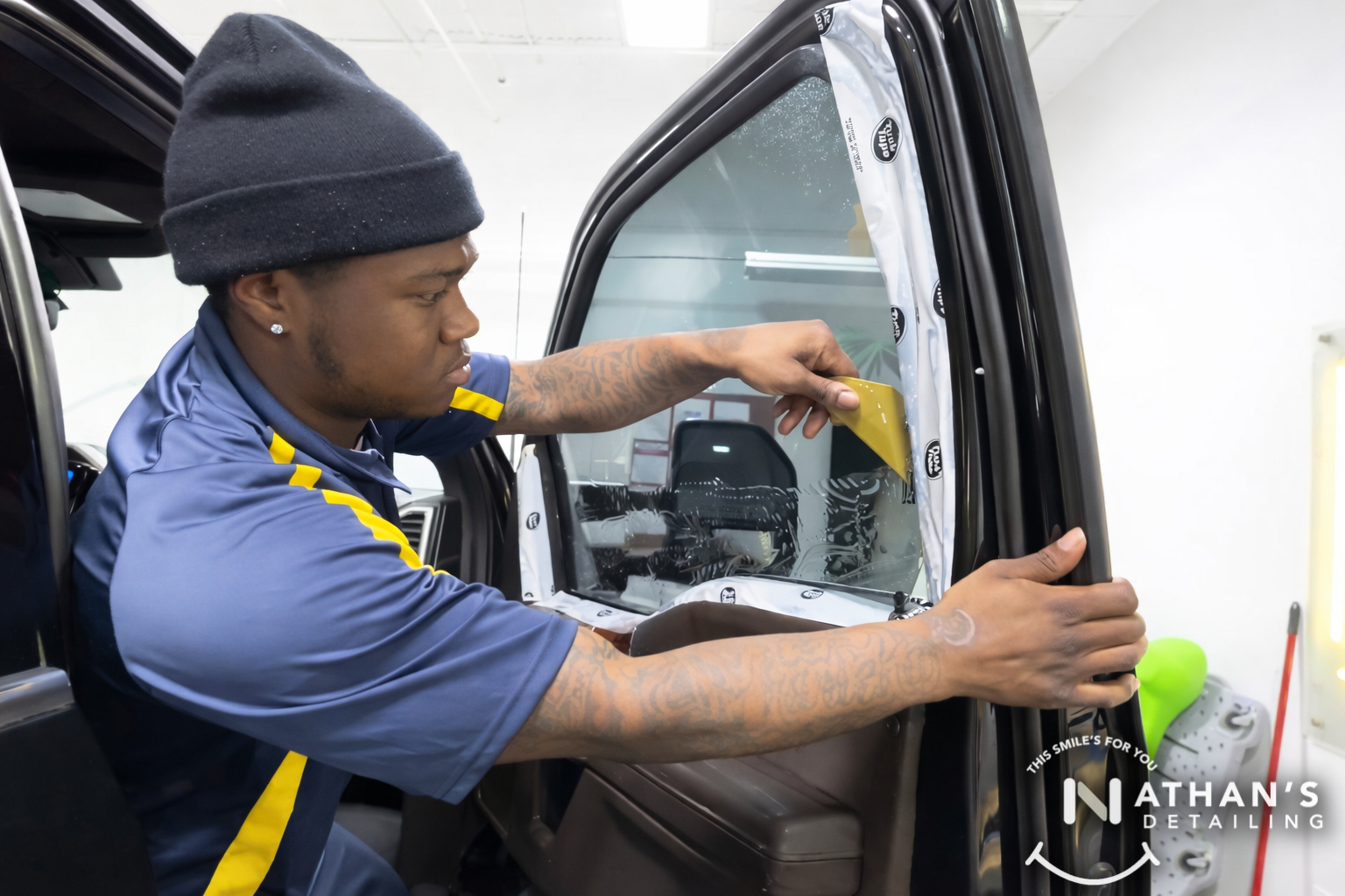Technician squeegeeing window tint film on an SUV door window during installation.
