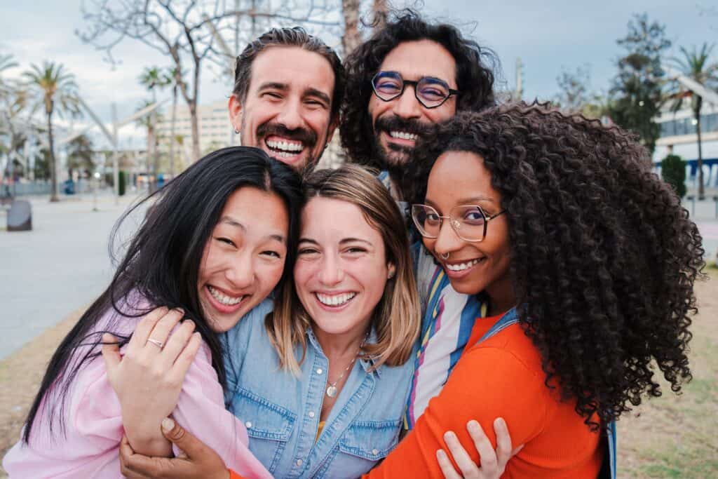 A joyful group of friends embracing each other and smiling at the camera in an outdoor urban setting.