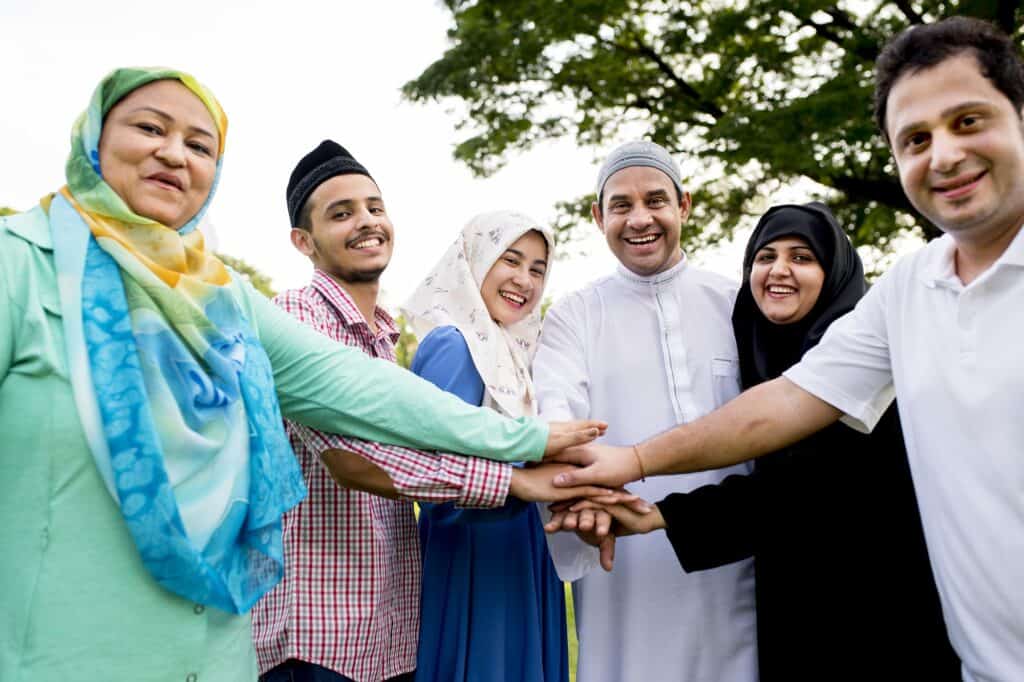 A Muslim group of smiling people, including men and women, standing together outdoors, stacking their hands in a show of unity and friendship