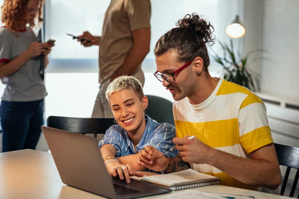 Two coworkers in a modern office, collaborating on a laptop.