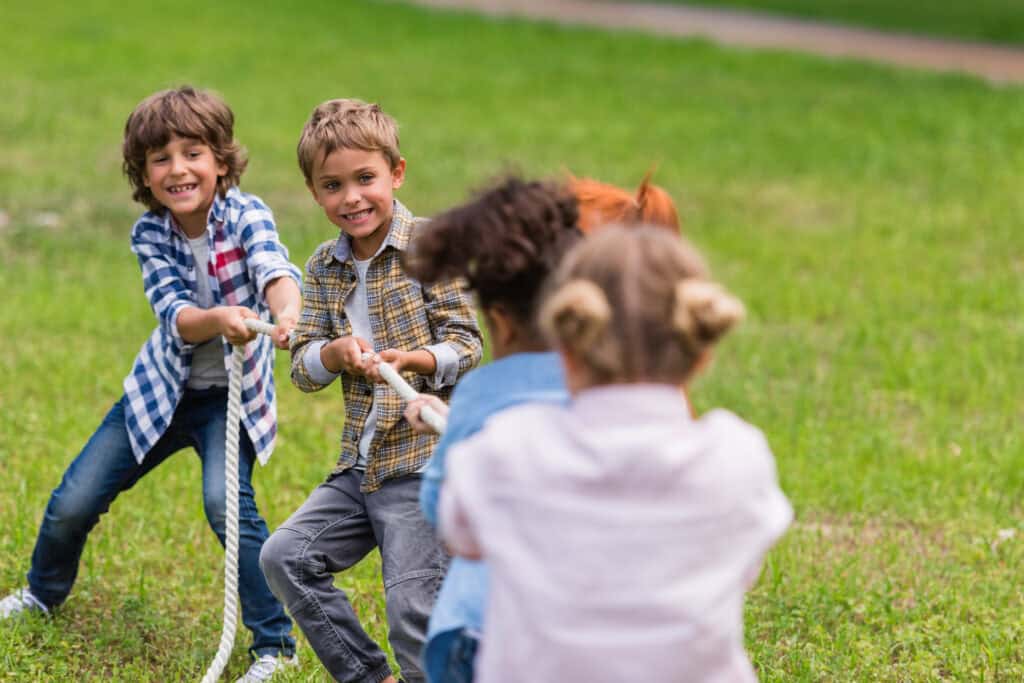 Smiling children compete in a tug-of-war game on the grass, pulling a rope with determination and teamwork.