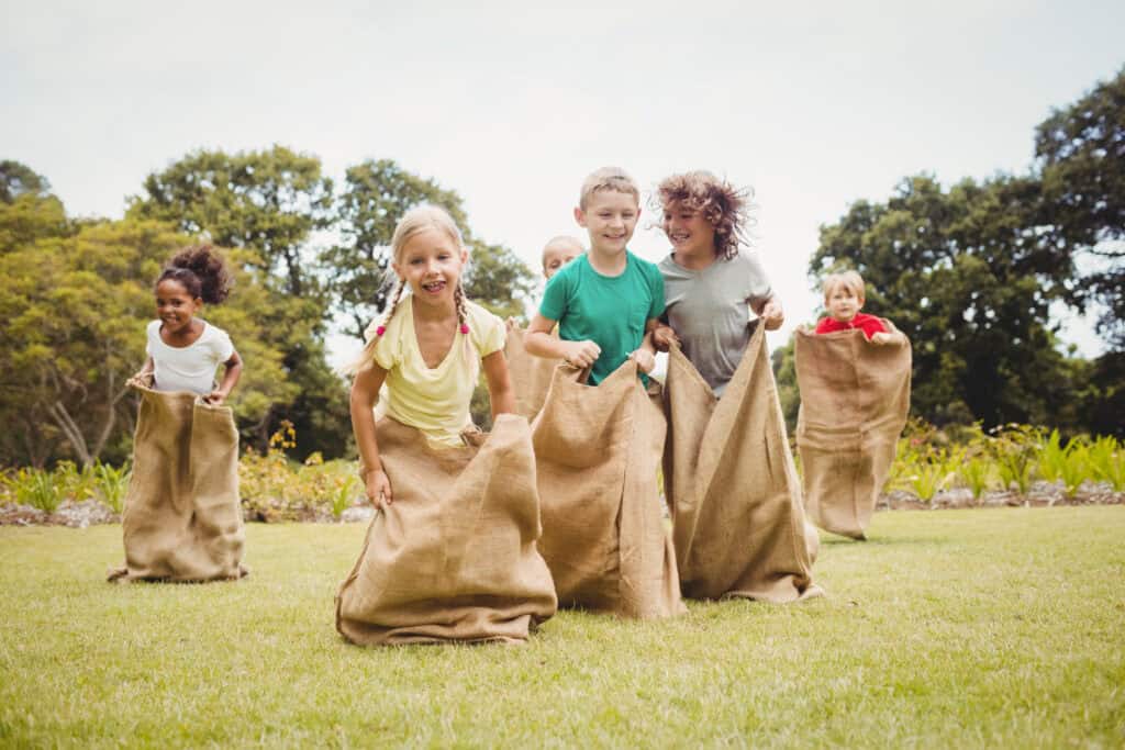 A joyful group of children participate in a sack race on a grassy field, laughing and competing with energy and excitement.