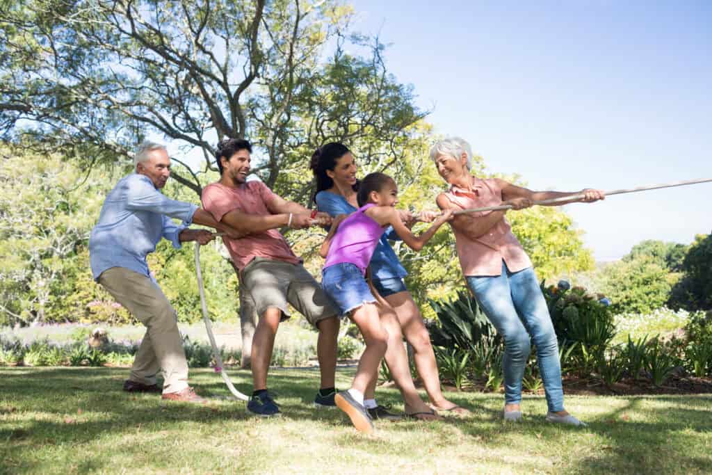 Multi-generational family enthusiastically playing tug-of-war on a sunny day in a park.
