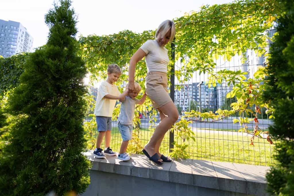 Mother walking on a low wall with her two young sons during a playful outdoor moment in the city.
