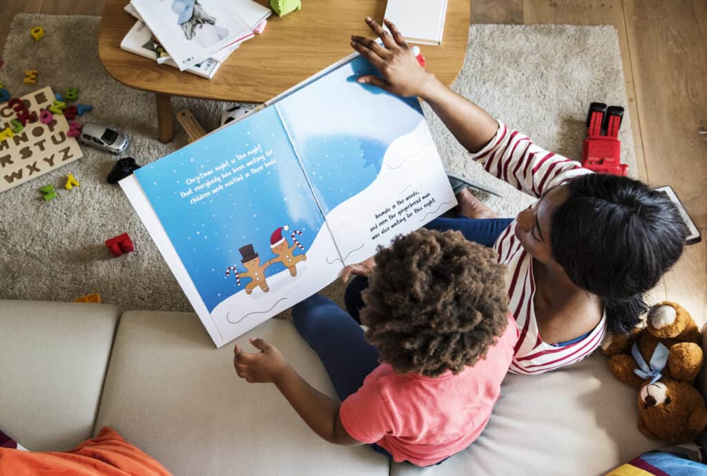 Mother and child reading a festive picture book with gingerbread characters, surrounded by toys and books in a cozy living room.