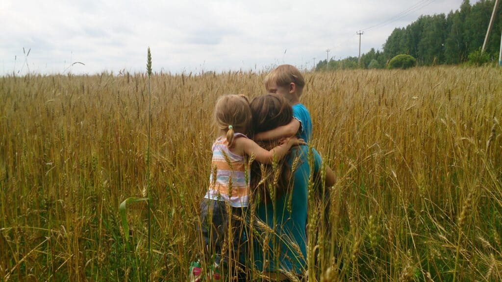 Mother hugging her two young children in the middle of a wheat field, showing deep affection.