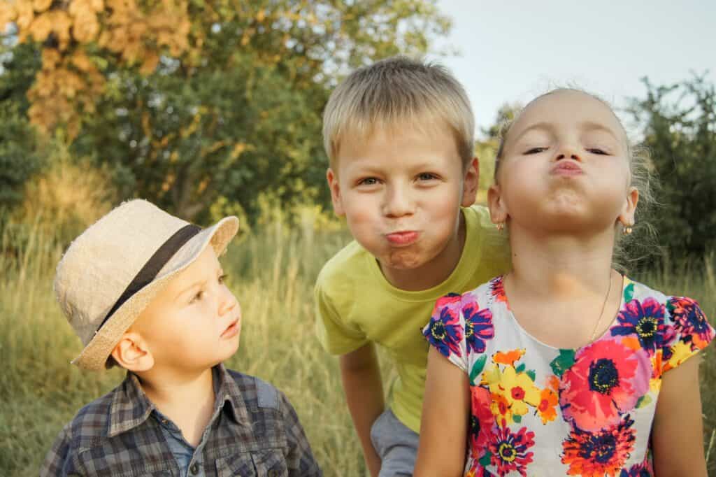 Group of children making playful faces in a grassy outdoor park.