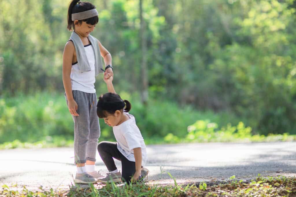 Older sister helping her younger sister get up after a fall during outdoor playtime.