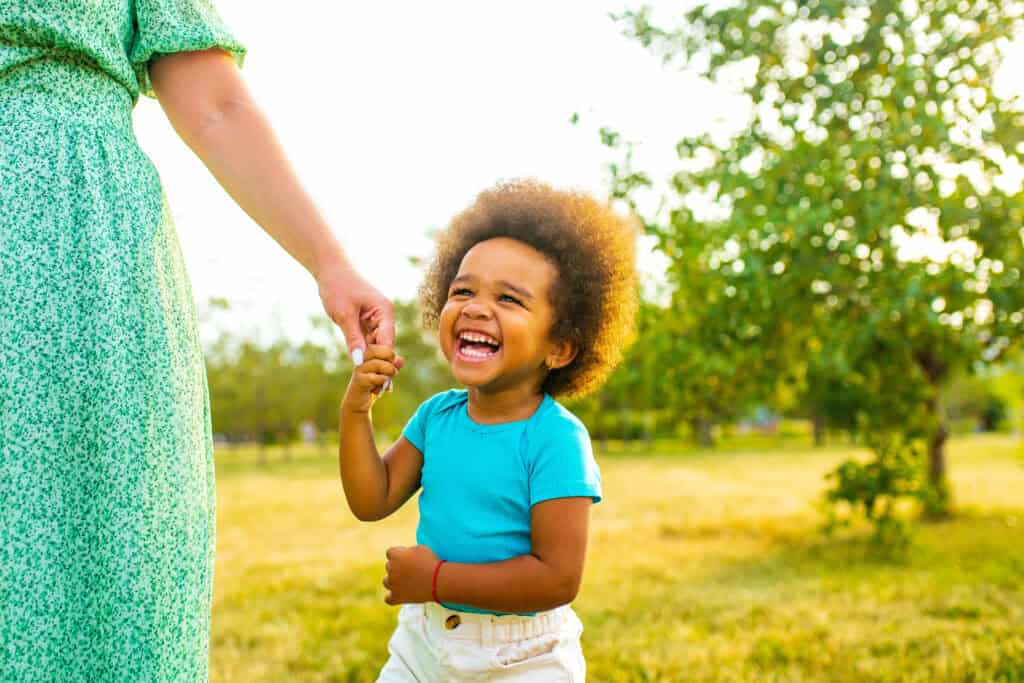 Laughing African-American girl holding a woman's hand in a sunny green park.