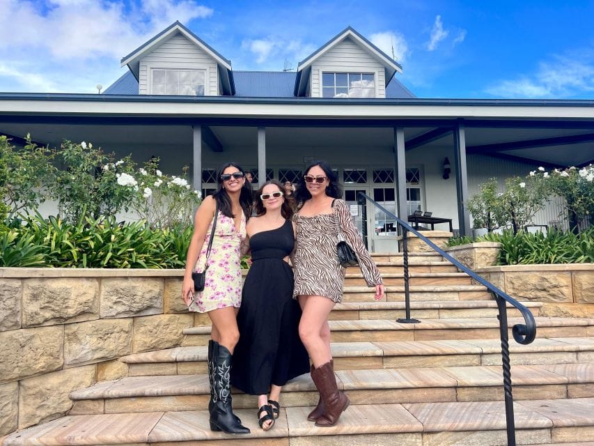 Group of women enjoying a Hunter Valley wine tour in front of a charming vineyard house, showcasing wine tasting and scenic vineyard views.