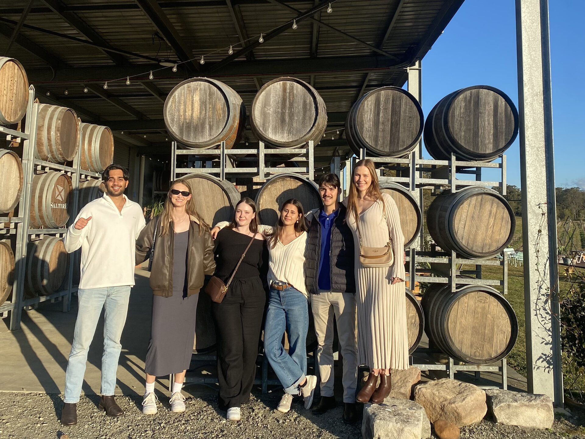 Group of friends enjoying wine tasting at Hunter Valley cellar, surrounded by wine barrels and scenic vineyard views. Perfect for wine lovers and tour enthusiasts.