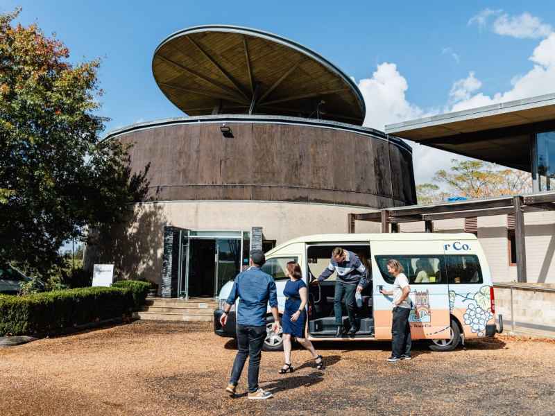 Modern tour van docking at a Newy Tour Co. location with travelers and staff preparing for a day of sightseeing in Newcastle, Australia.