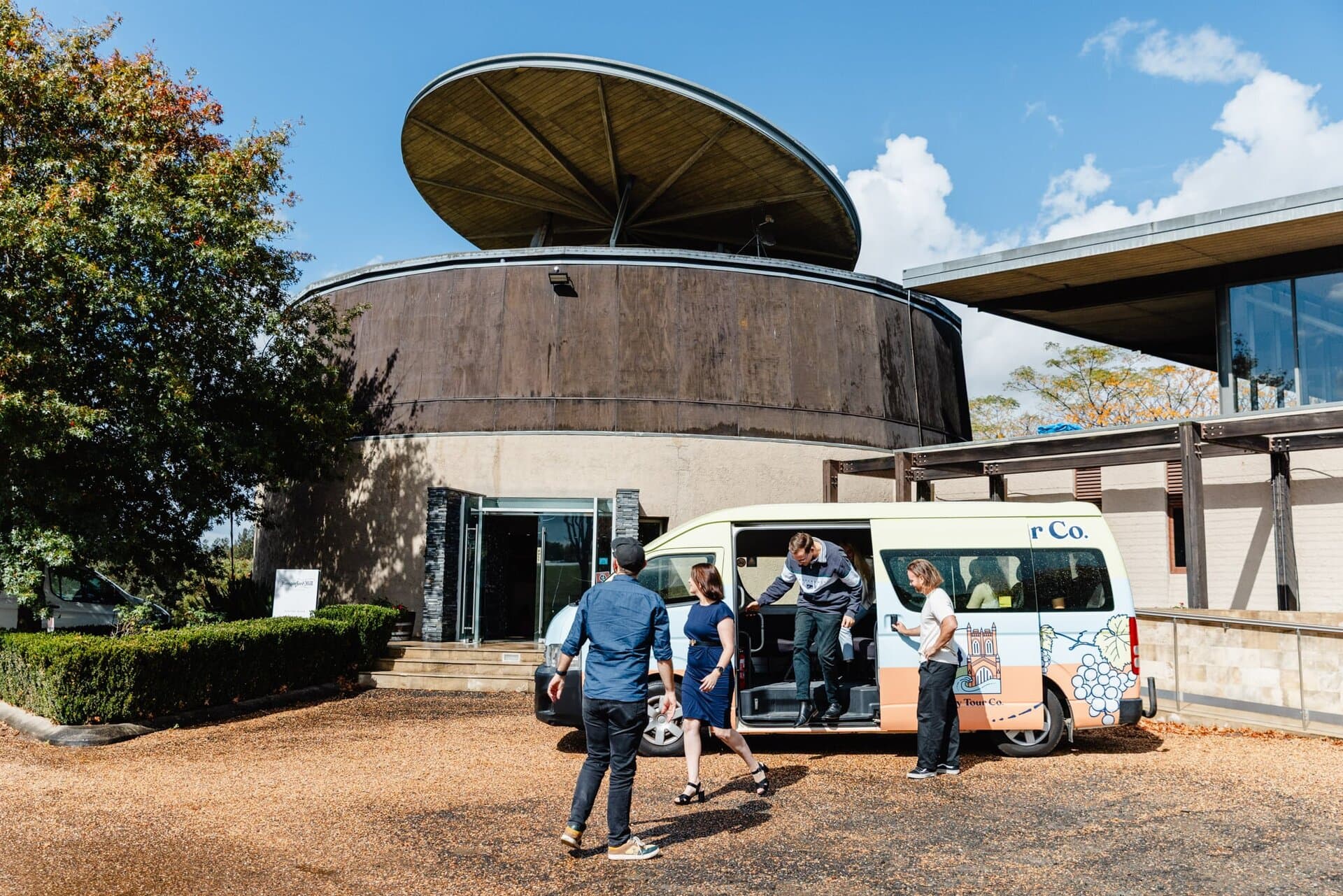 Modern tour van docking at a Newy Tour Co. location with travelers and staff preparing for a day of sightseeing in Newcastle, Australia.