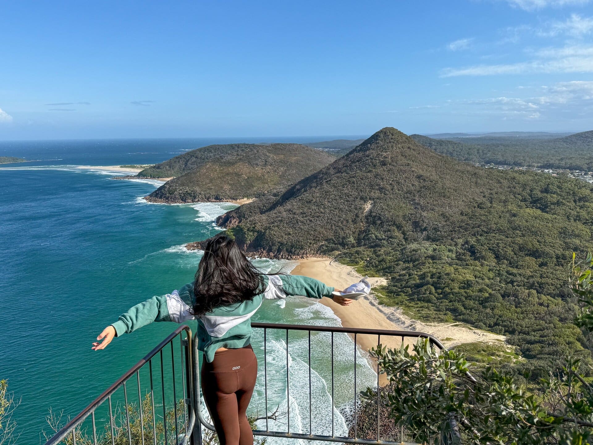 Breathtaking coastal view from a scenic lookout featuring a woman enjoying the panoramic landscape of Newy's beaches and lush green hills, perfect for tourists and adventure seekers.