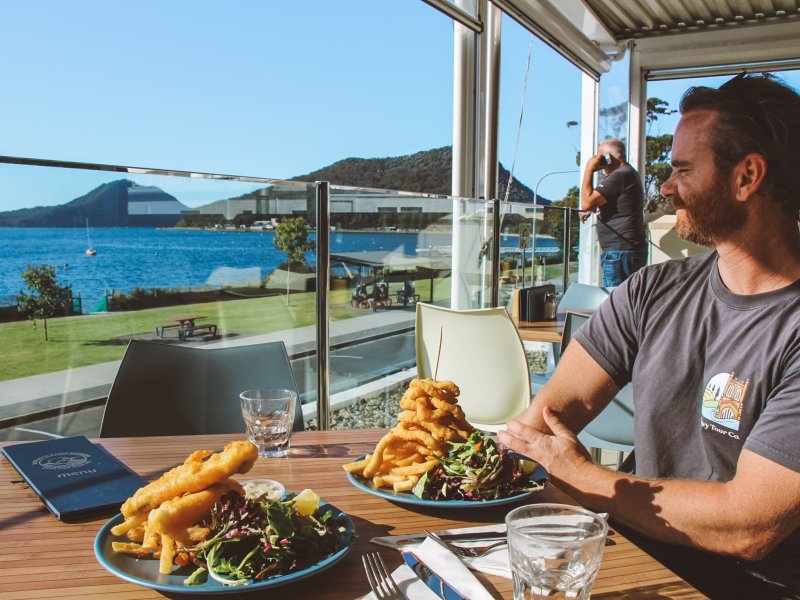 Man enjoying seafood lunch with ocean view at Port Stephens during private tour. Scenic outdoor dining with whales and hiking nearby.