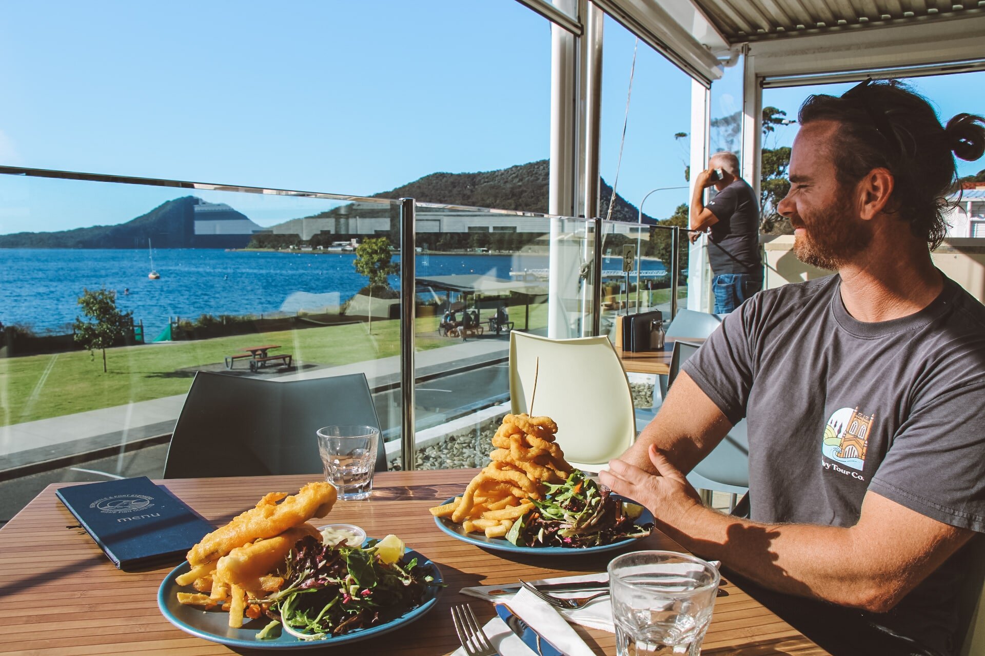 Man enjoying seafood lunch with ocean view at Port Stephens during private tour. Scenic outdoor dining with whales and hiking nearby.