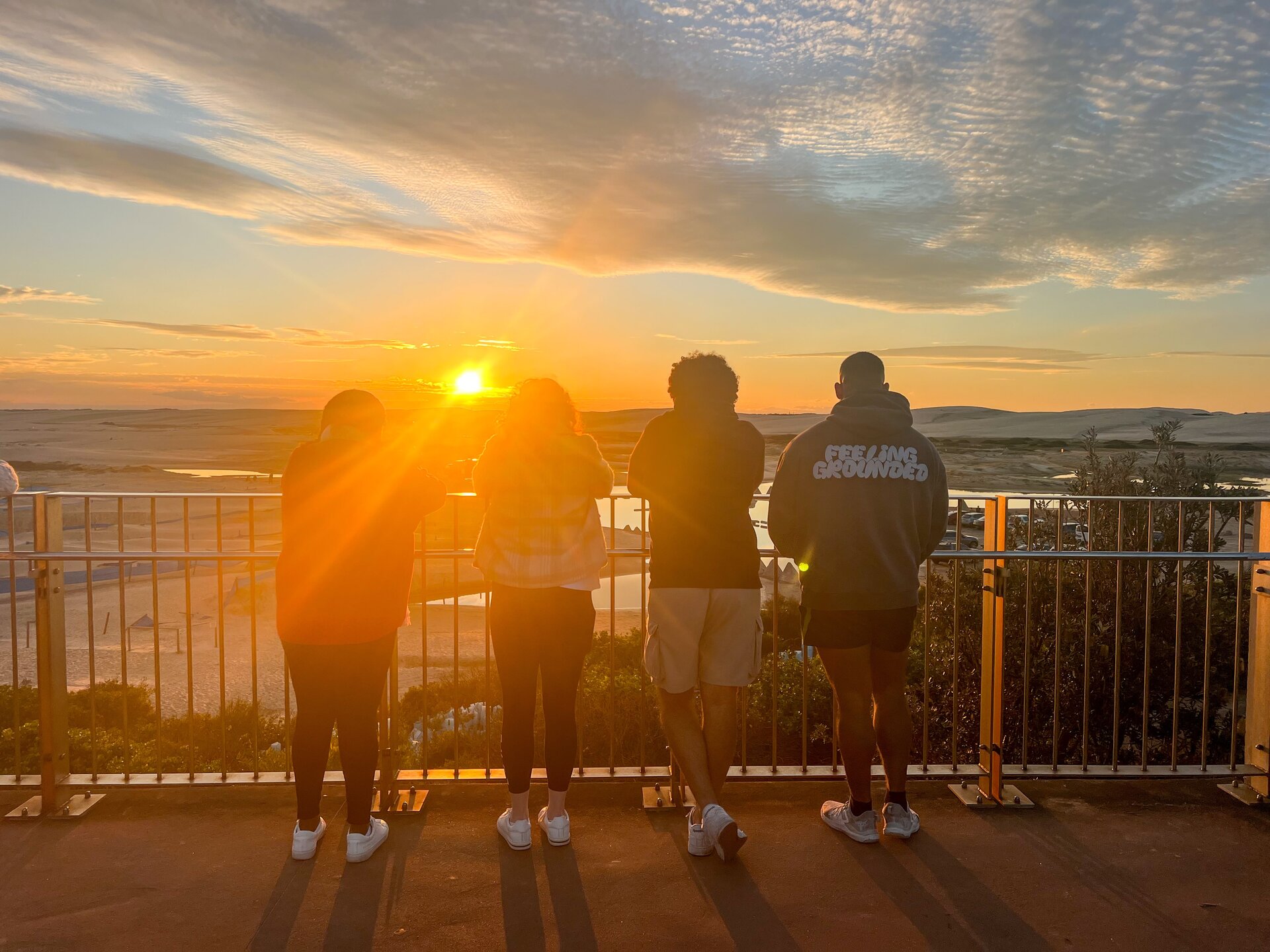 Group of four people enjoying a sunset view at Port Stephens during a private tour, with whales and hiking activities.