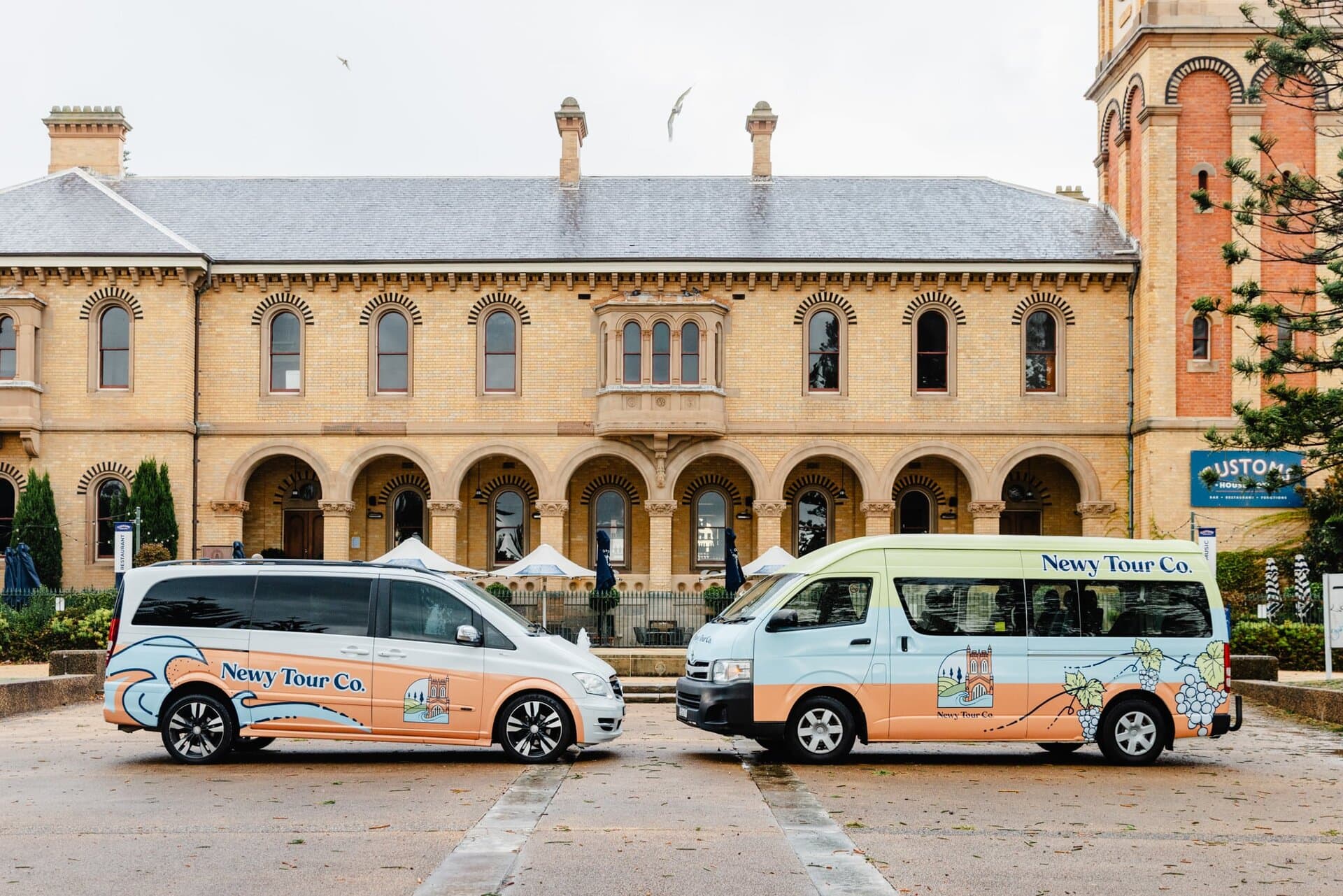 Luxury tour vans parked in front of historic building in Newcastle, Australia, showcasing Newy Tour Co. transportation services for wine tours, city sightseeing, and winery visits.