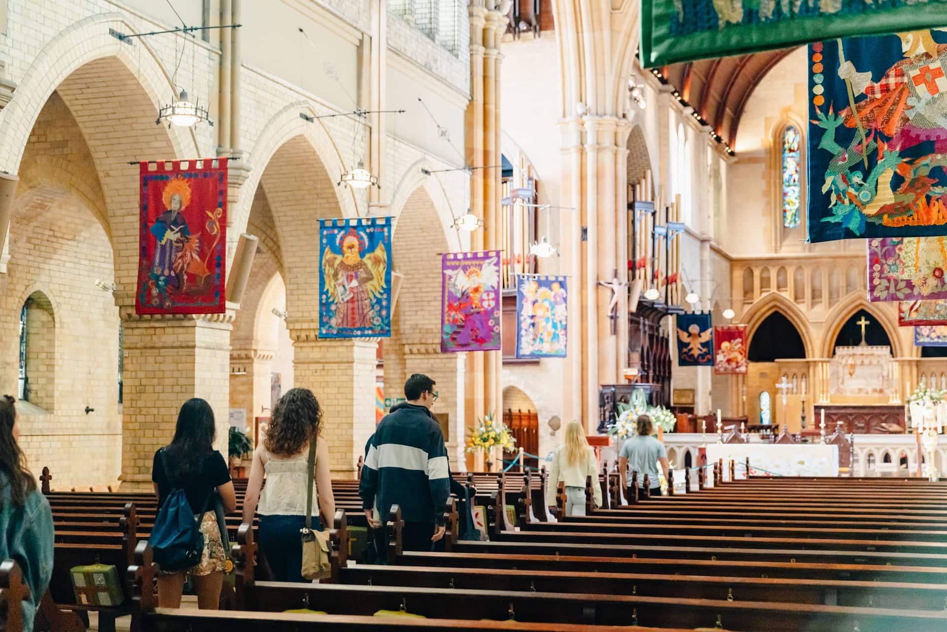 Colorful religious banners hanging inside a historic church with visitors walking down the aisle, showcasing architectural beauty, sacred atmosphere, and cultural heritage.