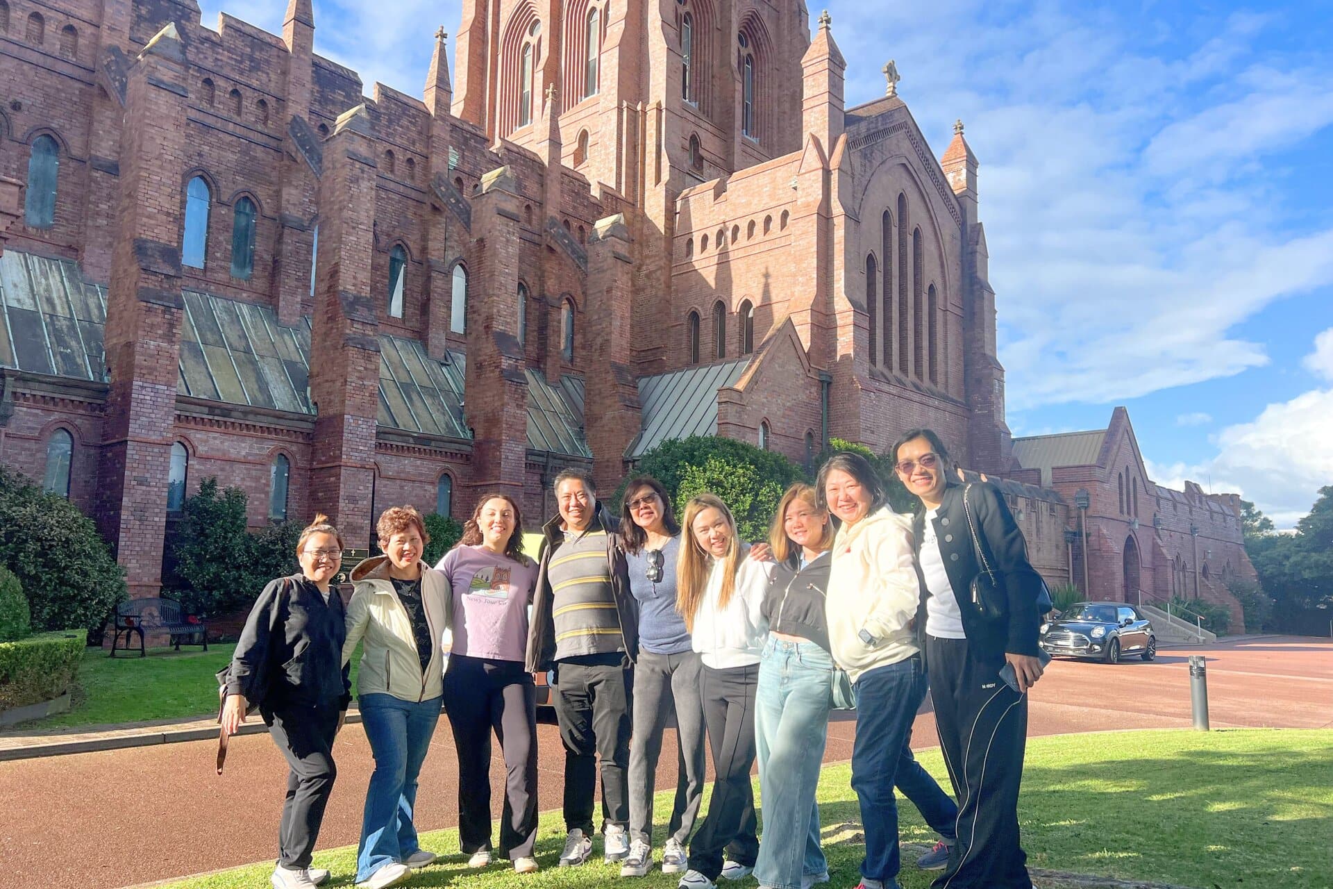 Historic Newcastle Cathedral with a group of smiling tourists in front, capturing fun sightseeing moments during Newy Tour Co. guided travel experiences.