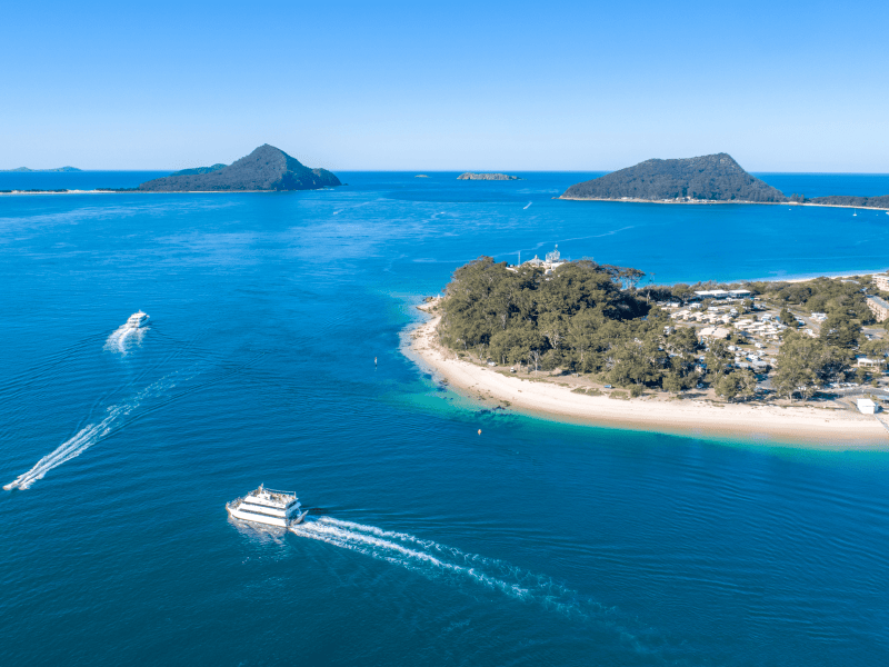 Breathtaking aerial view of Newcastle Harbour with boats sailing past a scenic island and vibrant blue waters, showcasing Newy Tour Co.'s top island tours and marine adventures in Newcastle, Australia.