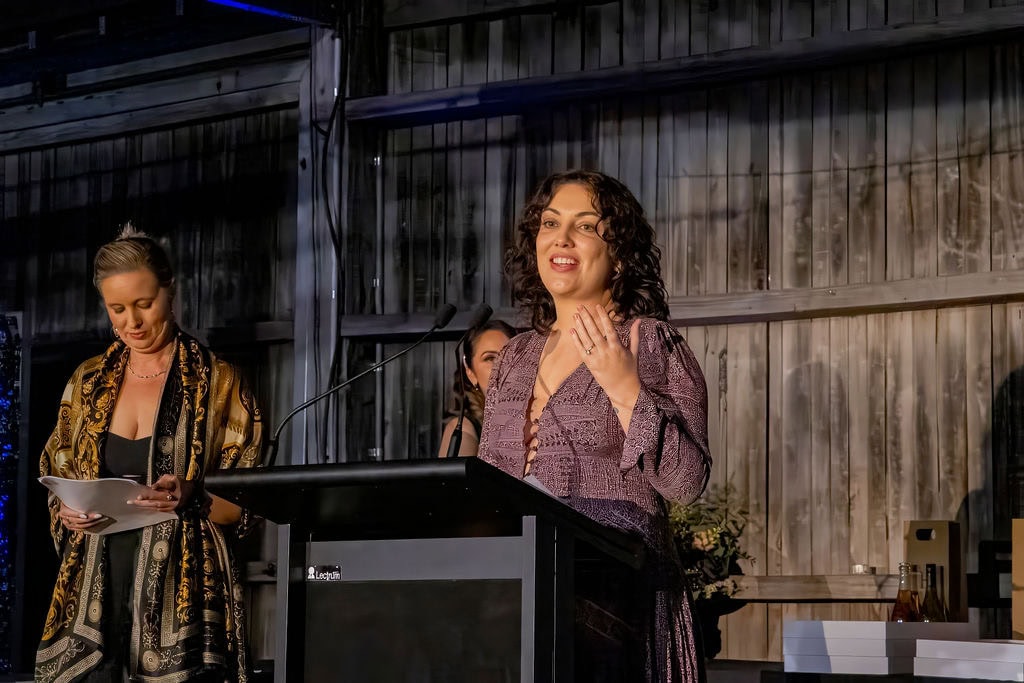 Vibrant woman giving speech at Newy Tour Co. event, promoting local tours and experiences in Newcastle, Australia, with a lively atmosphere and professional setting.
