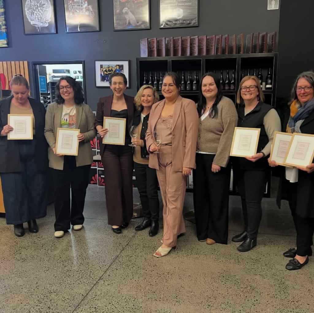 Awards ceremony celebrating team achievements at Newy Tour Co. in Newcastle, Australia, featuring smiling staff holding certificates and wine glasses, highlighting team success and company recognition.