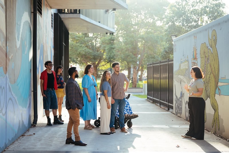 Group of tourists listening to a guide during a Newcastle street art and food tour, exploring vibrant murals and local cuisine in the city’s arts district.