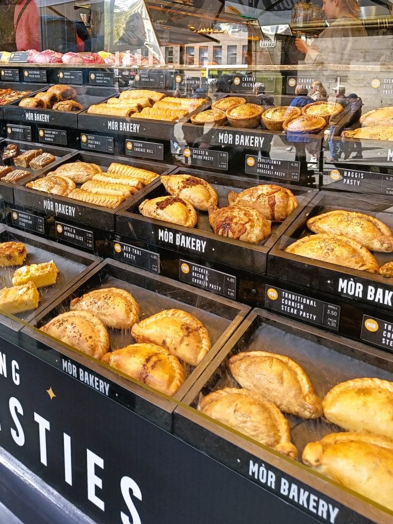 Bakery window display with various pasties and pastries neatly arranged in labeled trays, tempting visitors exploring the best attractions Edinburgh has to offer.