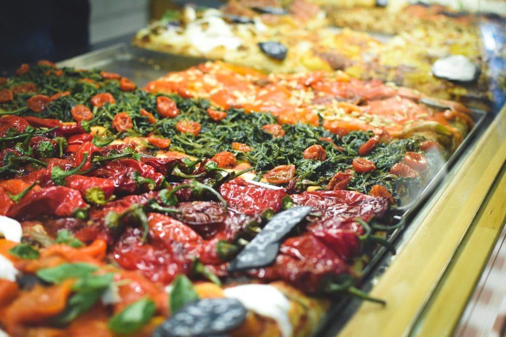 A must-try display of assorted pizzas with colorful toppings, including red peppers, greens, and tomatoes, showcases the vibrant flavors of Italian cuisine.