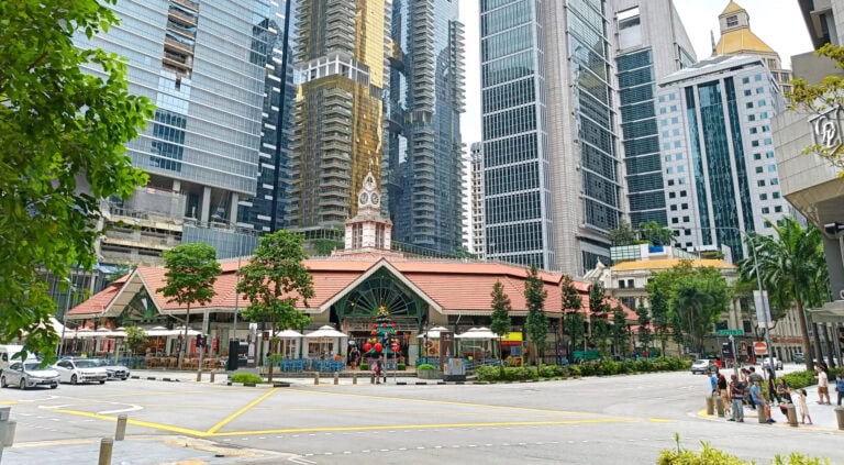 Discover Satay Street and the iconic Lau Pa Sat Hawker market in Singapore, set against a cityscape of tall modern buildings that frame its charming red roof and clock tower.