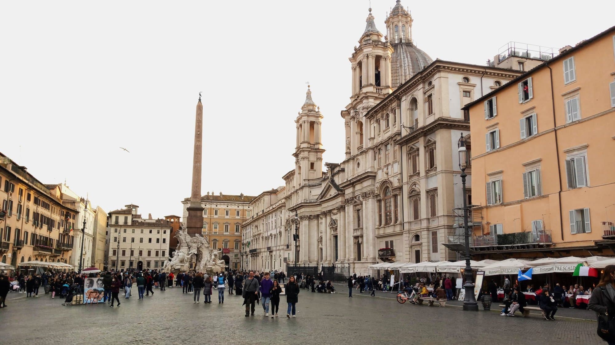 Piazza Navona, one of the must-see attractions in Rome, buzzes with crowds admiring its historic buildings and towering obelisk under a clear sky.