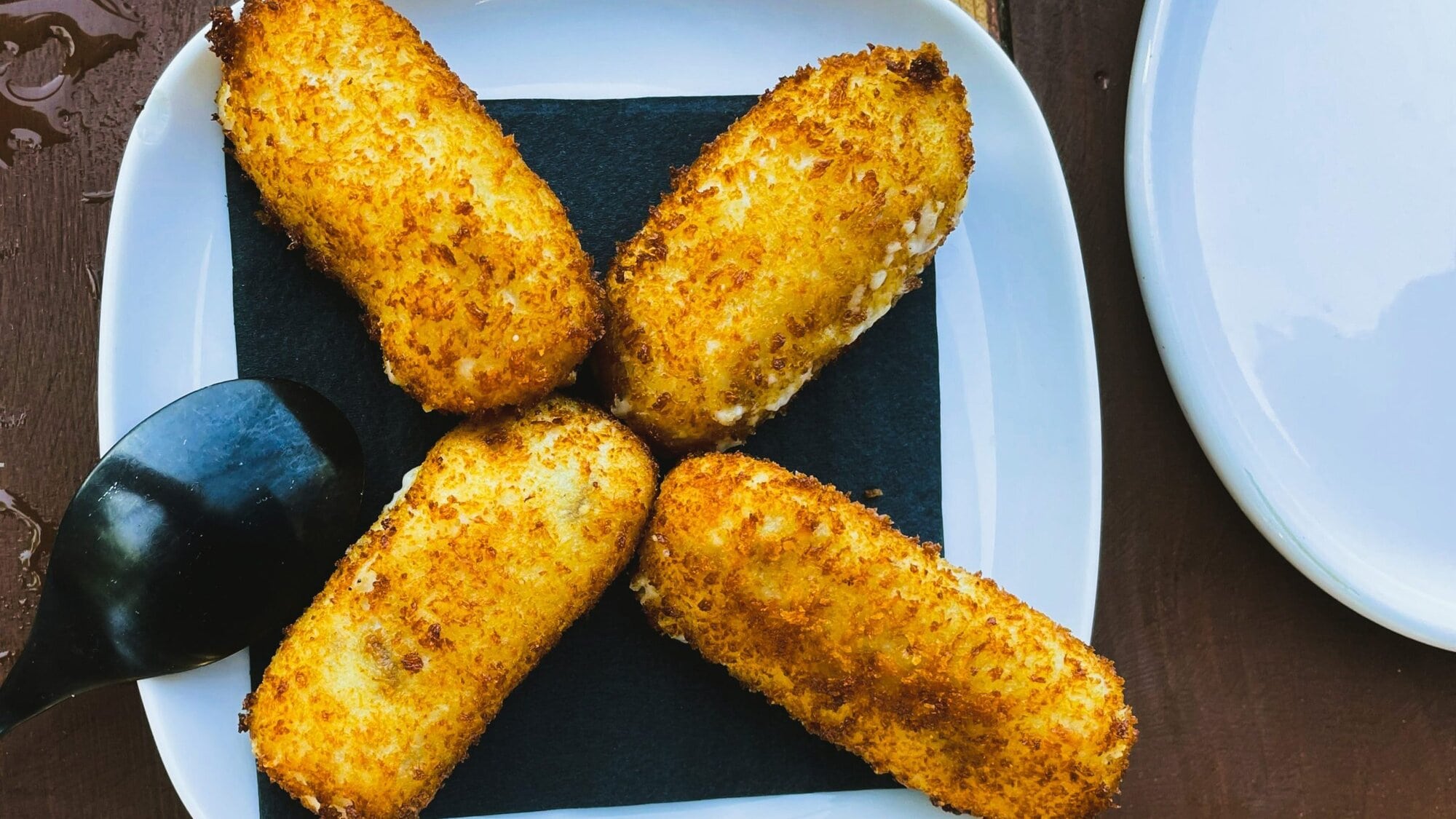 Four must-try crispy croquettes sit elegantly on a white plate with a black napkin and spoon, offering a delightful taste of Italian cuisine.